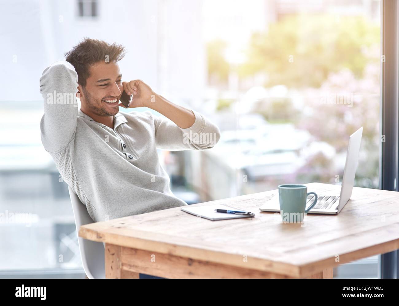 L'auto-emploi a ses avantages : un jeune entrepreneur parlant sur son téléphone portable dans son bureau. Banque D'Images