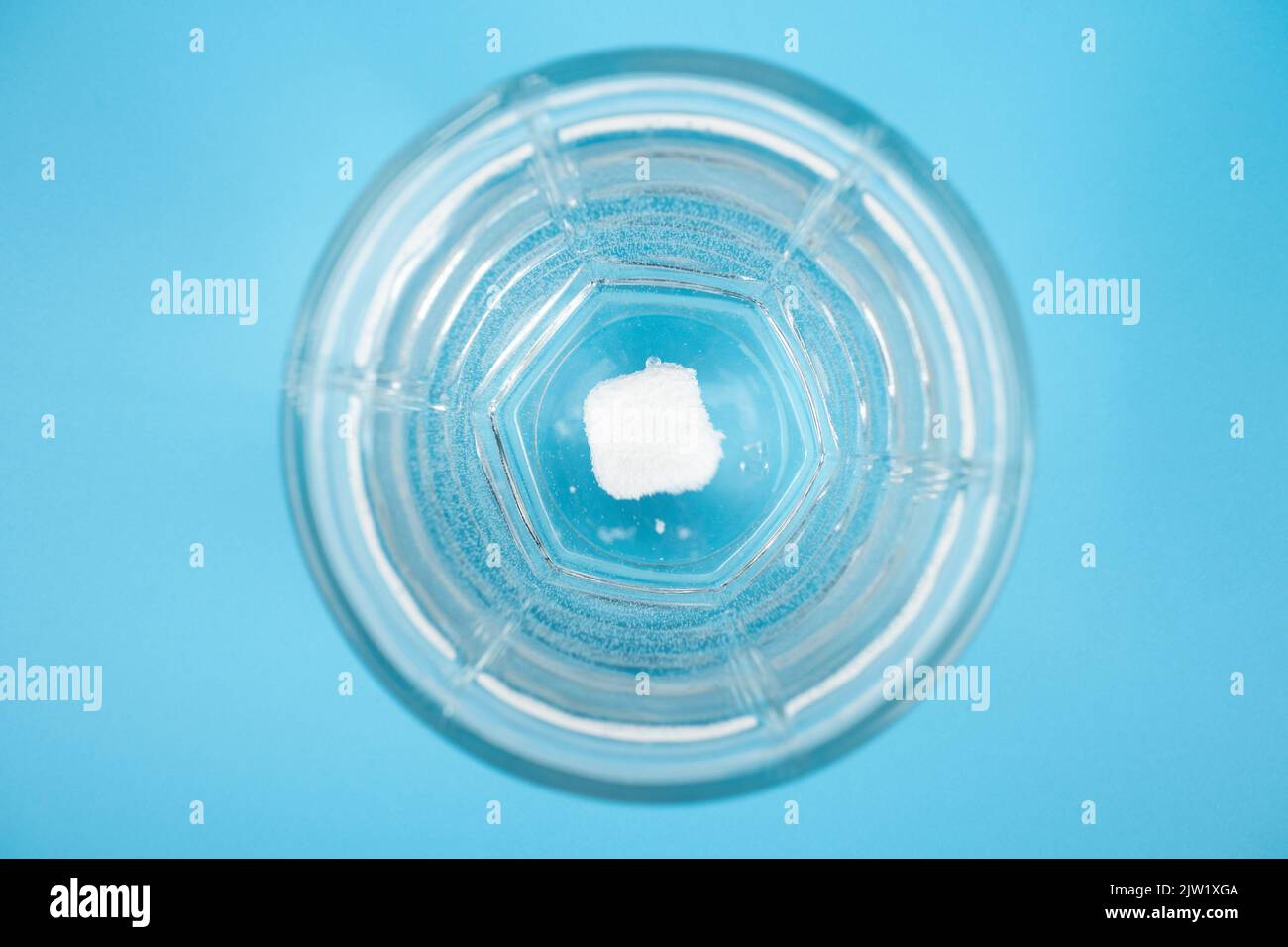 la pilule se dissout dans un verre d'eau sur un fond bleu vue du dessus. Banque D'Images