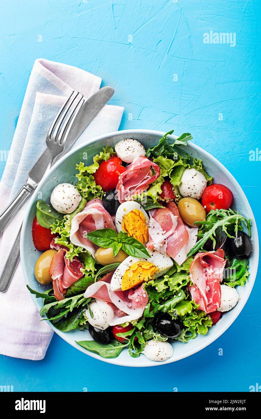 Salade verte saine avec prosciutto, mozzarella, œuf, olives et tomate sur fond bleu Banque D'Images