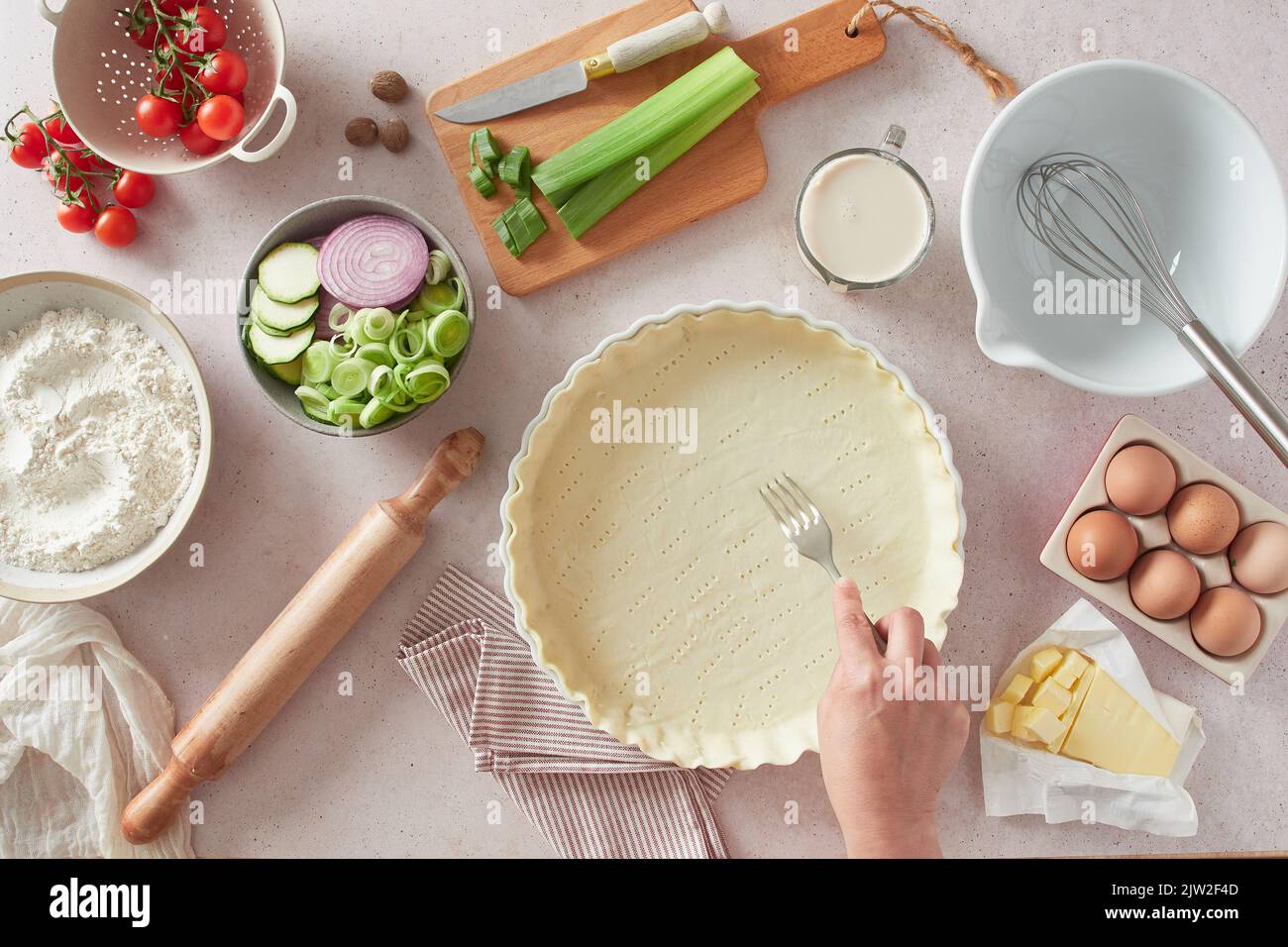 Vue de dessus de la femelle anonyme utilisant la fourchette pour ancrer des trous dans la croûte de quiche crue près des ustensiles de cuisine et des ingrédients frais sur la table dans la cuisine Banque D'Images