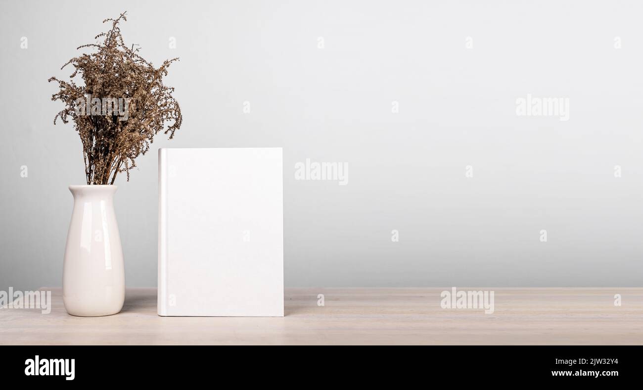 Bannière avec maquette de livre et bouquet de fleurs séchées dans un vase au bureau. Magnifique et tendre intérieur de l'amateur de lecture dans un style minimaliste. Roman avec le blan Banque D'Images