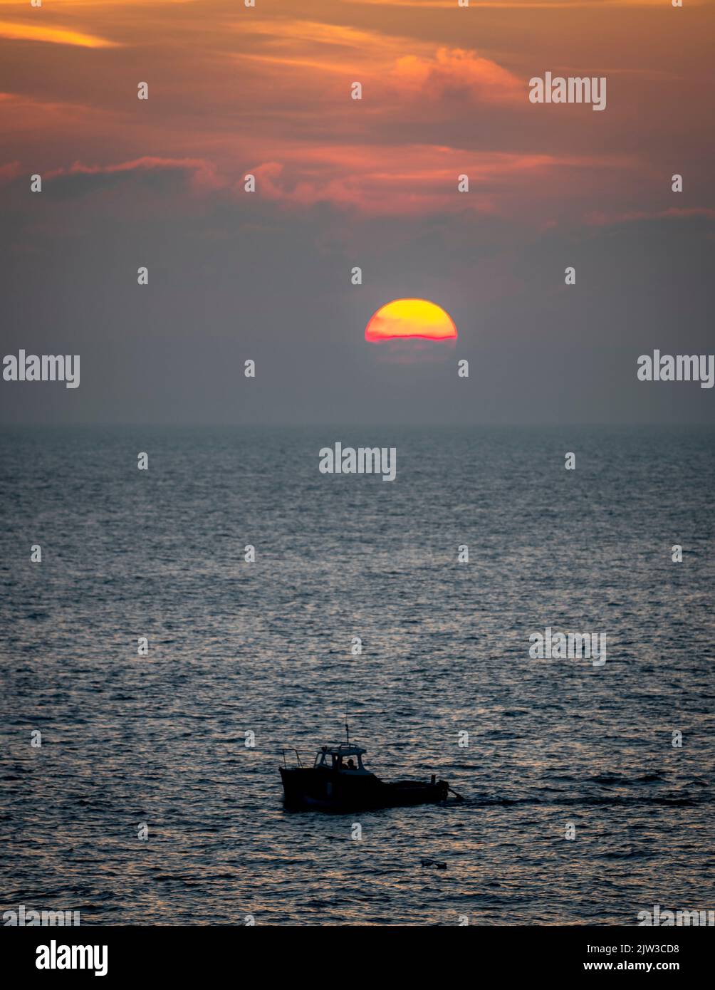 Bateau de pêche qui rentre à la maison après une dure journée de pêche avec le soleil se coucher à l'horizon. Banque D'Images