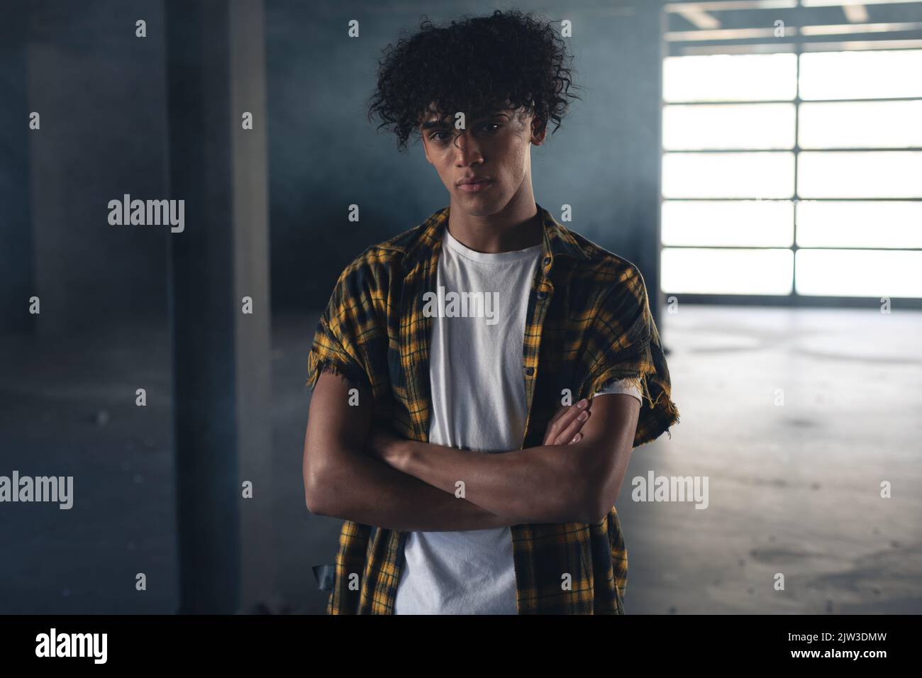 Portrait d'homme de course mixte dans un bâtiment vide avec les bras croisés en regardant l'appareil photo Banque D'Images