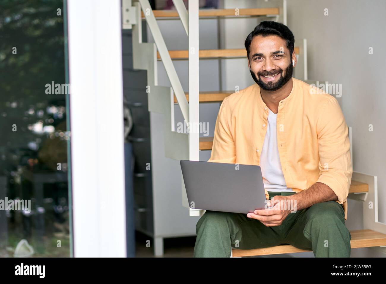 Homme indien souriant assis dans les escaliers à l'aide d'un ordinateur portable. Portrait Banque D'Images
