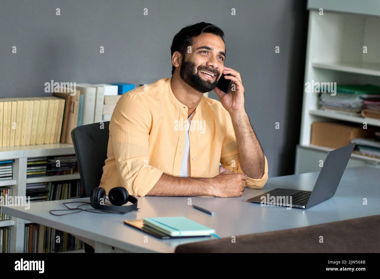 Un homme d'affaires indien heureux assis au bureau parlant au téléphone pour passer un appel. Banque D'Images