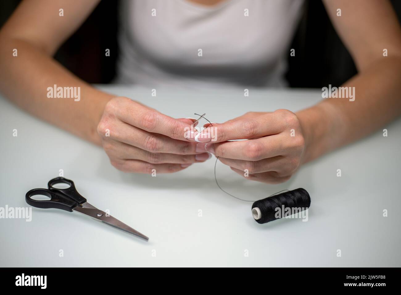 Femme filant l'aiguille à coudre à la table, gros plan. Banque D'Images