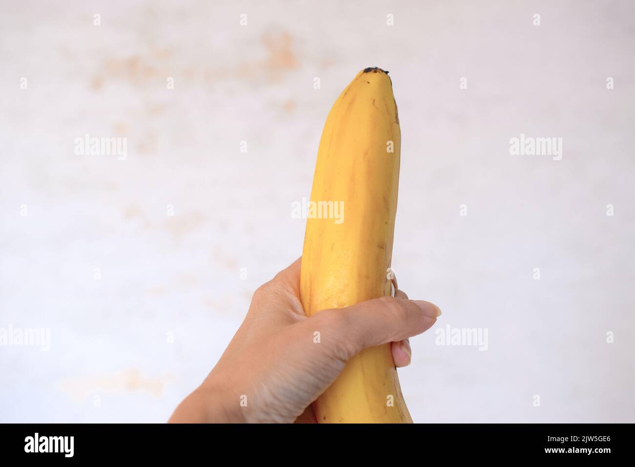 Banane dans une main femelle sur fond clair. Banque D'Images