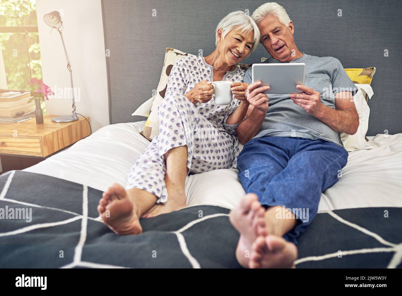 La maison est où votre coeur est. Un couple senior utilisant une tablette tout en étant allongé dans le lit. Banque D'Images