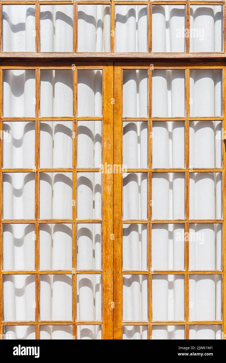 Treillis en bois de fenêtre panoramique le jour ensoleillé avec rideaux blancs fermés. Vider l'immense fenêtre du sol au plafond sur tout le mur, personne, l'espace intérieur Banque D'Images