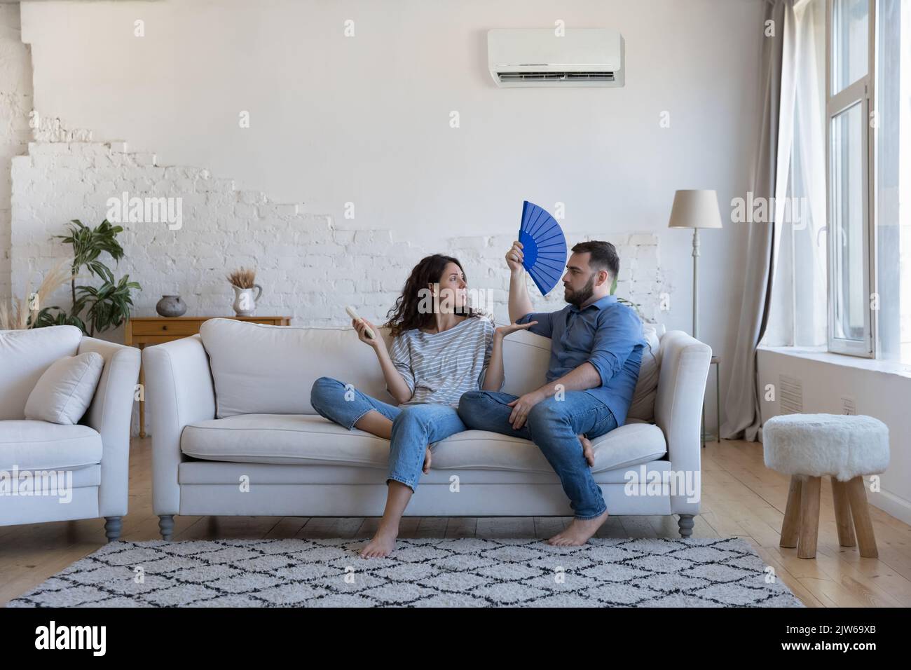 Un couple mécontent s'assoit sur un canapé avec ventilateur et télécommande Banque D'Images
