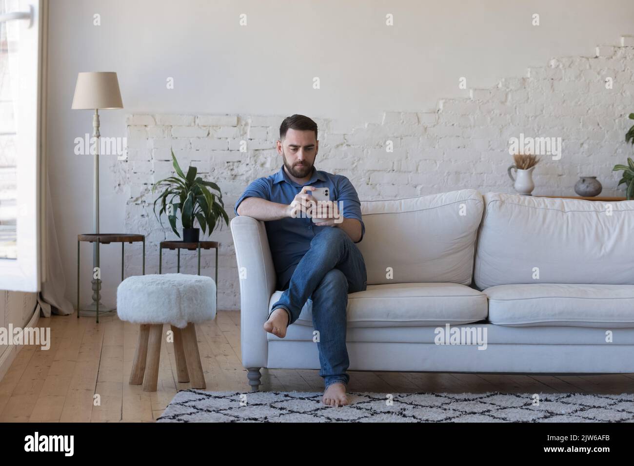 Homme sérieux utilisant un téléphone portable moderne assis sur un canapé Banque D'Images