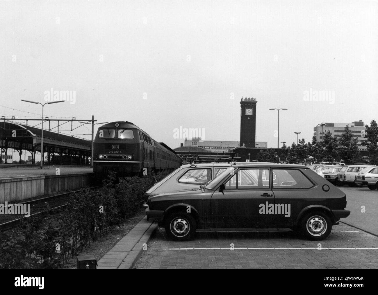 Vue sur la place de stationnement P+R à la gare de N.S. Nijmegen à Nijmegen avec le train pour Kleve (Allemagne) sur la gauche par la dieselocomotive 215 022-5 de la D.B. Et en arrière-plan le bâtiment de la gare. Banque D'Images