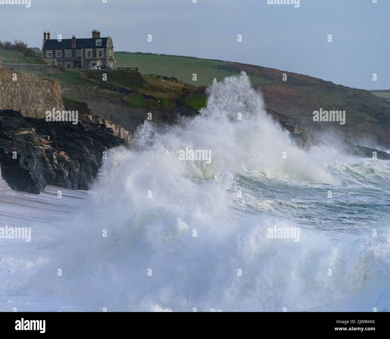 Des vagues massives se sont envolantes sur la plage de Porthleven avec Tye Rock Manor perché sur la falaise derrière. Banque D'Images