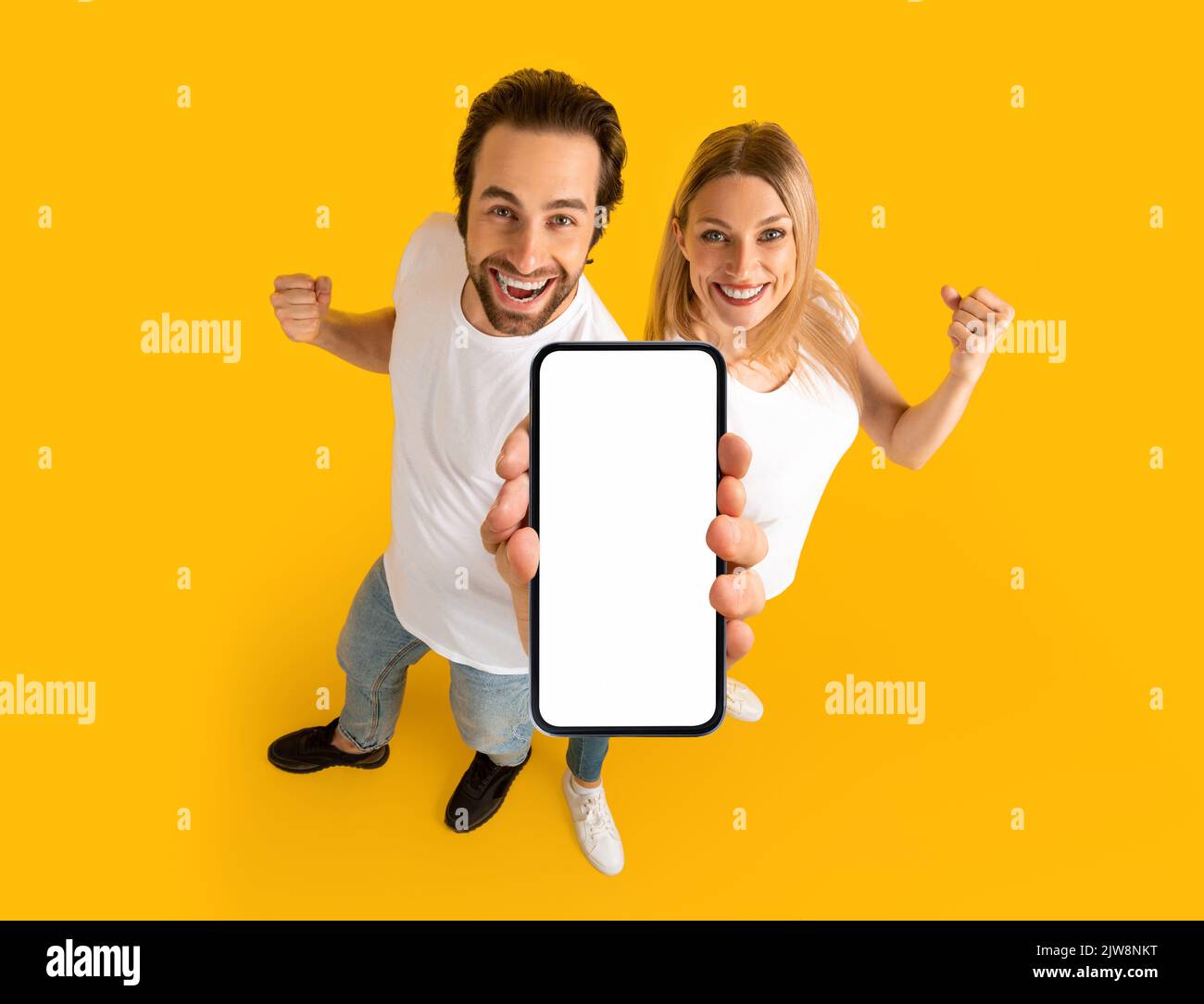 Joyeux couple de caucasiens du millénaire en t-shirts blancs, profitez de gagner en ligne, montrez votre smartphone avec un écran vierge Banque D'Images