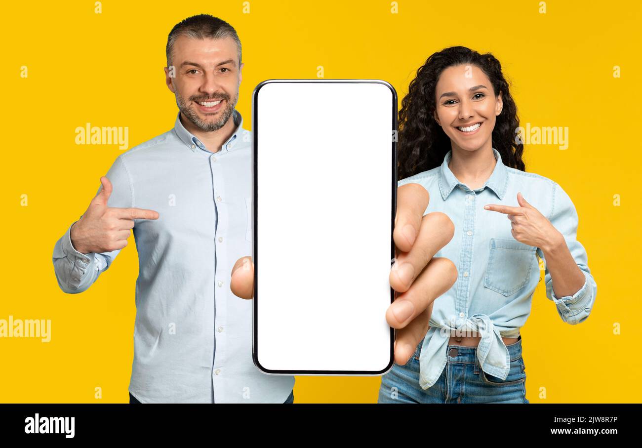 Un homme et une femme souriants, un homme et une femme, un doigt sur un grand smartphone avec un écran vide Banque D'Images