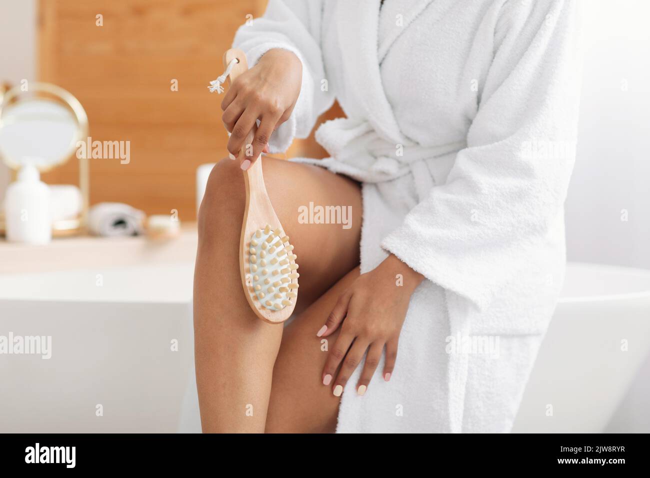 Femme massant les jambes à l'aide d'une brosse en bois dans la salle de bains, court Banque D'Images