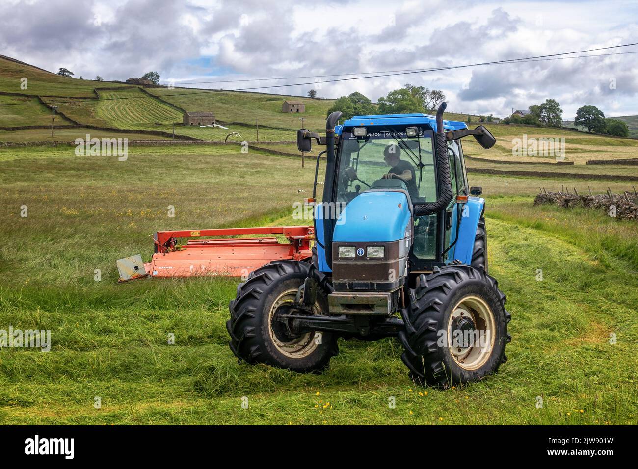 Gros plan d'un agriculteur dans un tracteur bleu qui coupe l'herbe pour l'ensilage dans les champs près d'Appletreewick dans le parc national de Yorkshire Dales, Angleterre, Royaume-Uni Banque D'Images