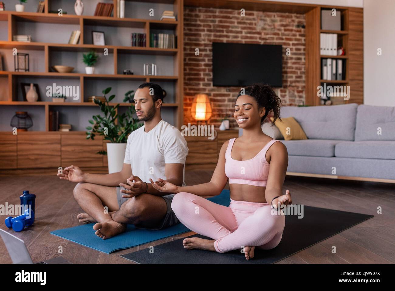 Joyeux calme jeune africain américain mari et femme dans sportswear méditer ou pratiquer le yoga sur mat Banque D'Images