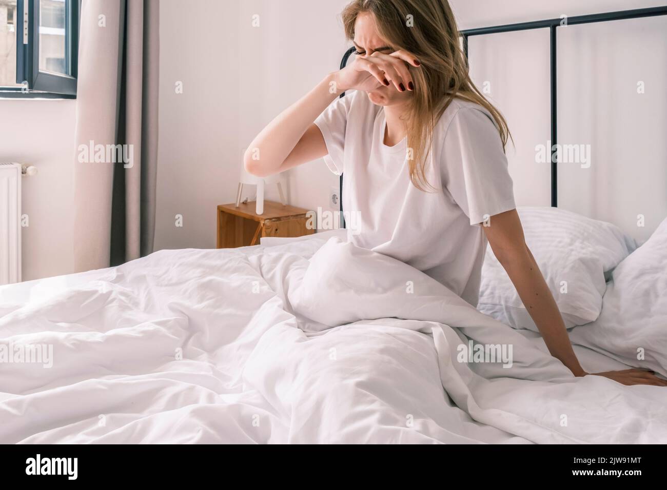 Une jeune femme endormi frotte les yeux tout en étant assise dans le lit le matin se sentant fatiguée après se réveiller. Mauvais sommeil agité. Stress, cauchemars Banque D'Images