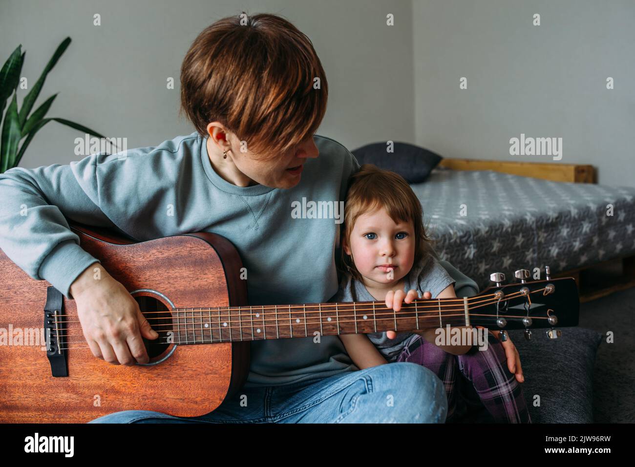 Une petite fille joue de la guitare avec sa mère sur le sol à la maison Banque D'Images