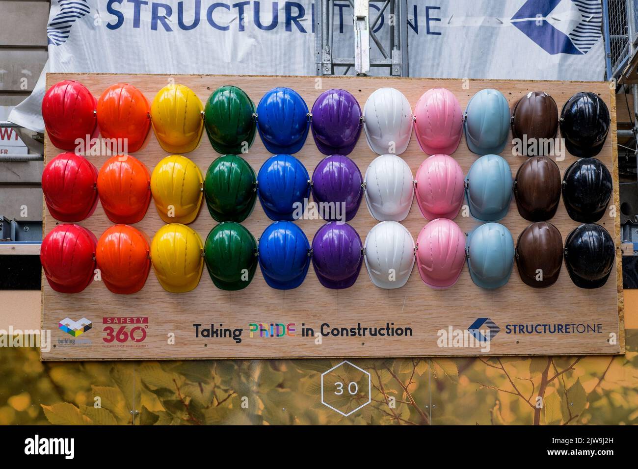 Présentation des casques de sécurité des travailleurs dans des couleurs arc-en-ciel représentant le concept d'inclusion au sein de la main-d'œuvre de l'industrie de la construction, Londres, Royaume-Uni. Banque D'Images