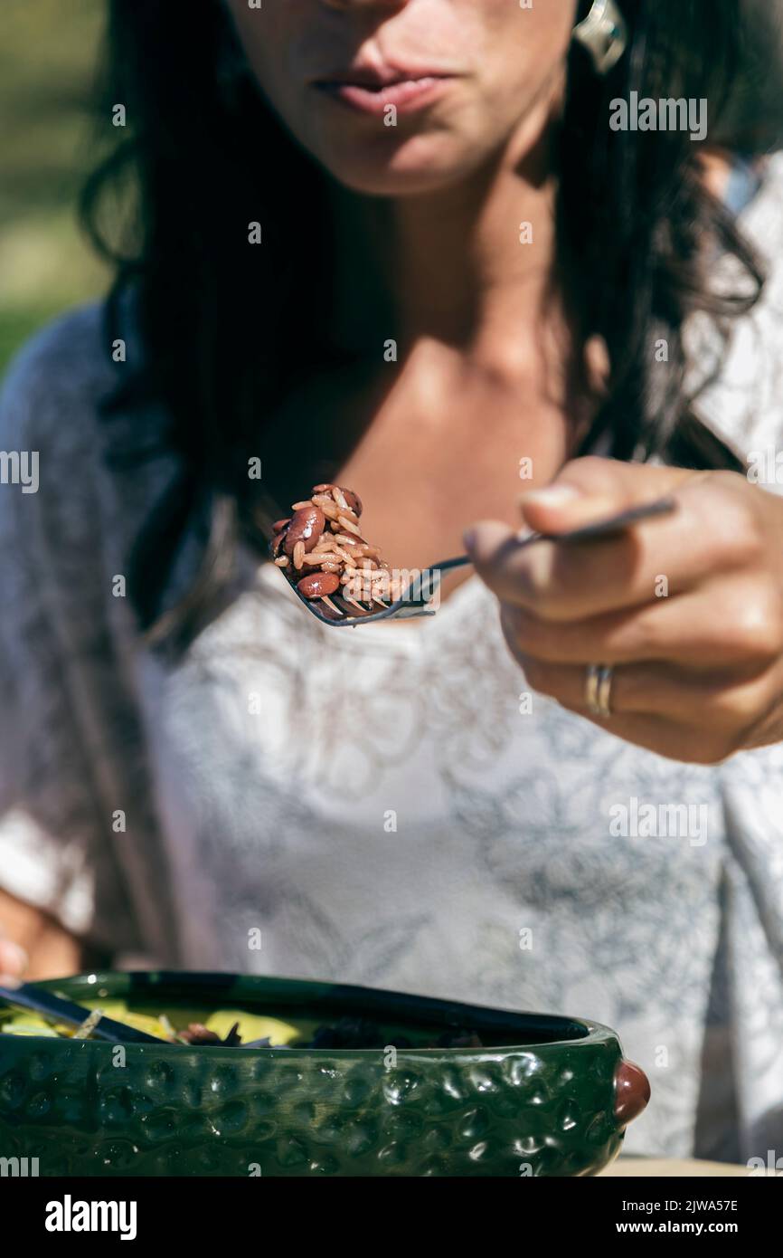 Femme mangeant du riz avec des haricots. Elle tient une fourchette dans sa main et la pointe vers sa bouche. Les vibes tropicales Banque D'Images