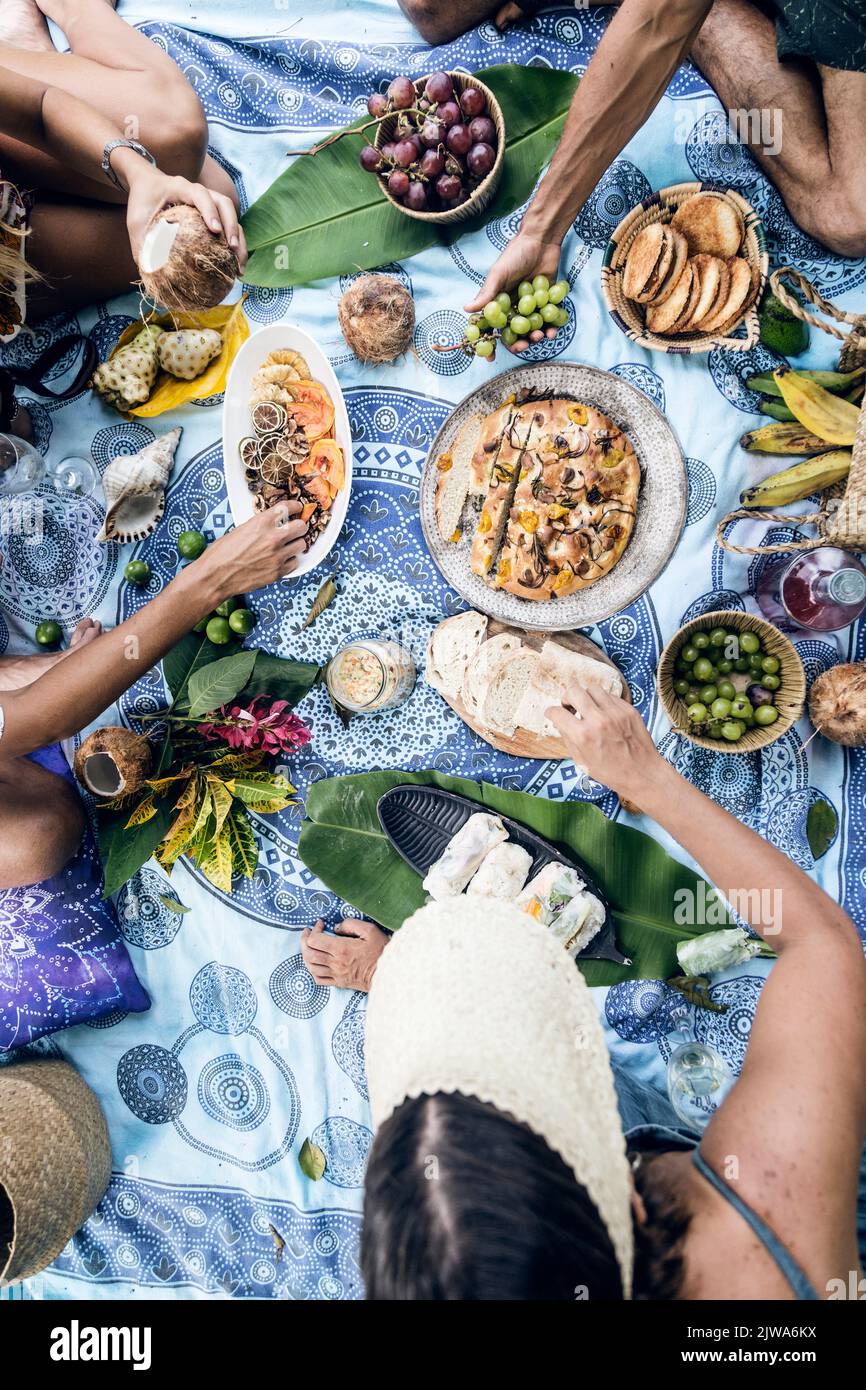 Amis ayant un pique-nique sur une nappe bleue avec beaucoup de nourriture et de boissons. Atmosphère détendue dans la nature. Des vibes d'été Banque D'Images