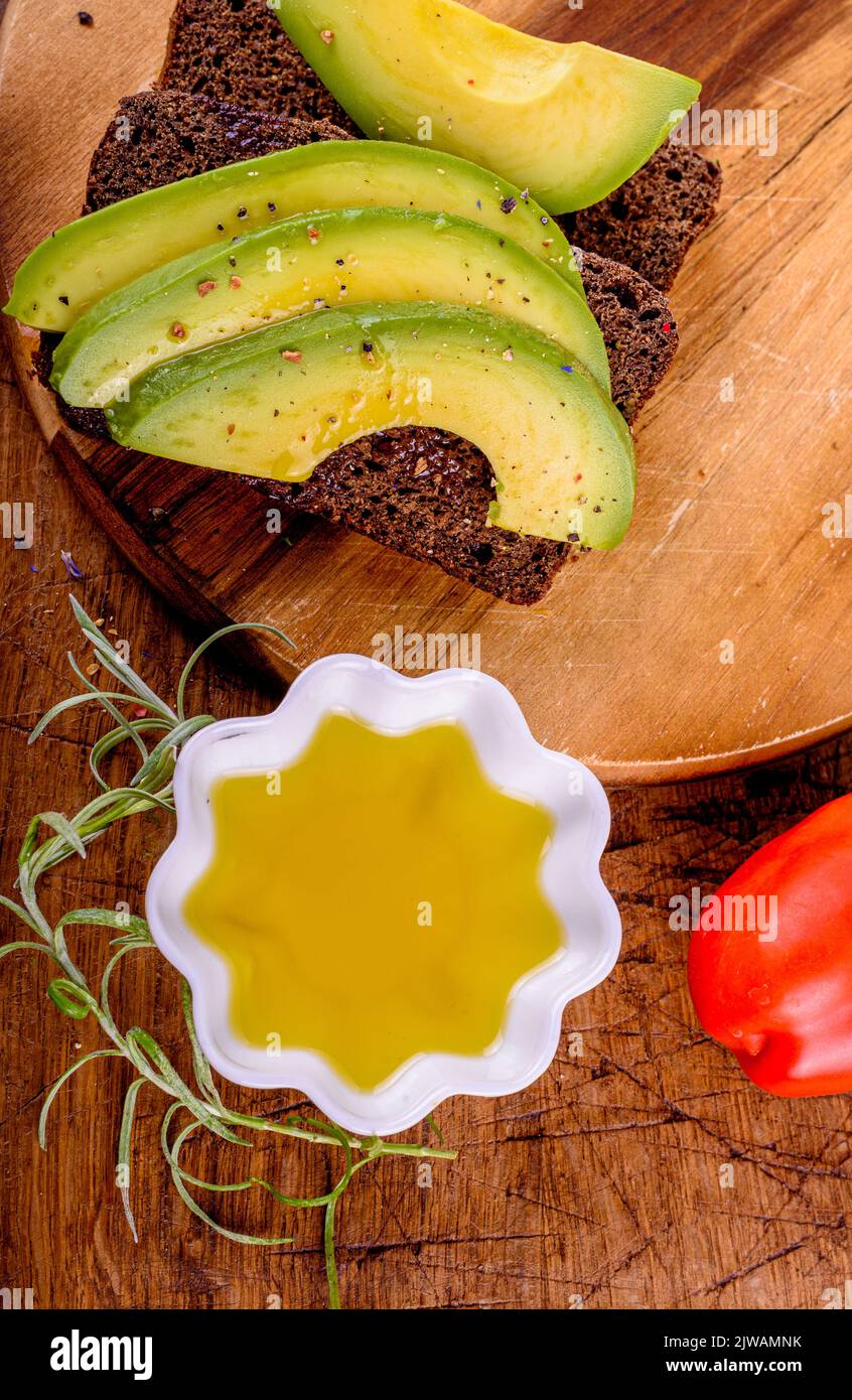 Huile d'olive en tasse blanche, tomate rouge, pain de seigle avec avocat sur planche à découper. Banque D'Images
