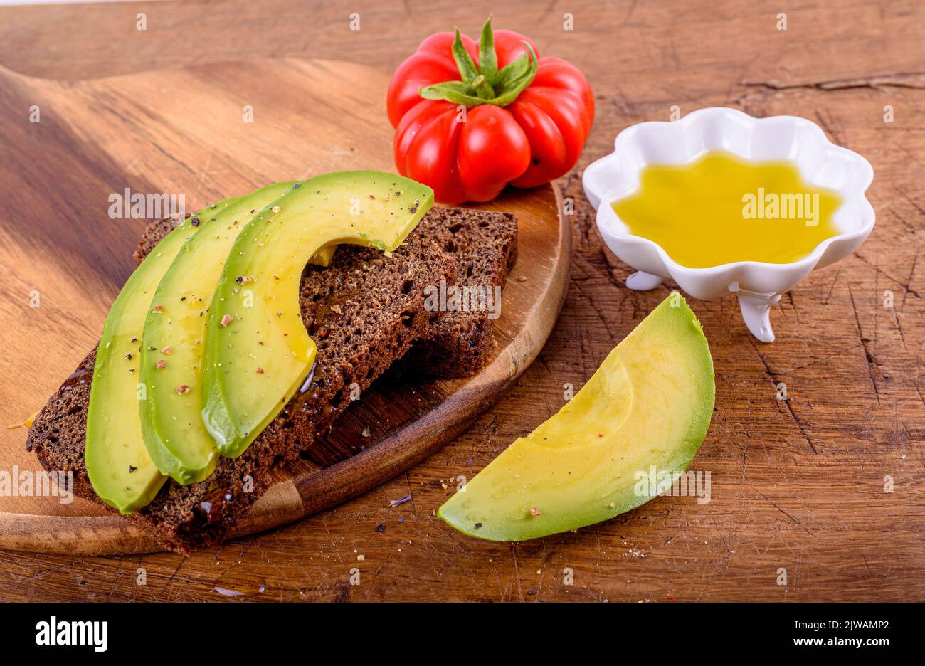 Huile d'olive en tasse blanche, tomate rouge, pain de seigle avec avocat sur planche à découper. Banque D'Images
