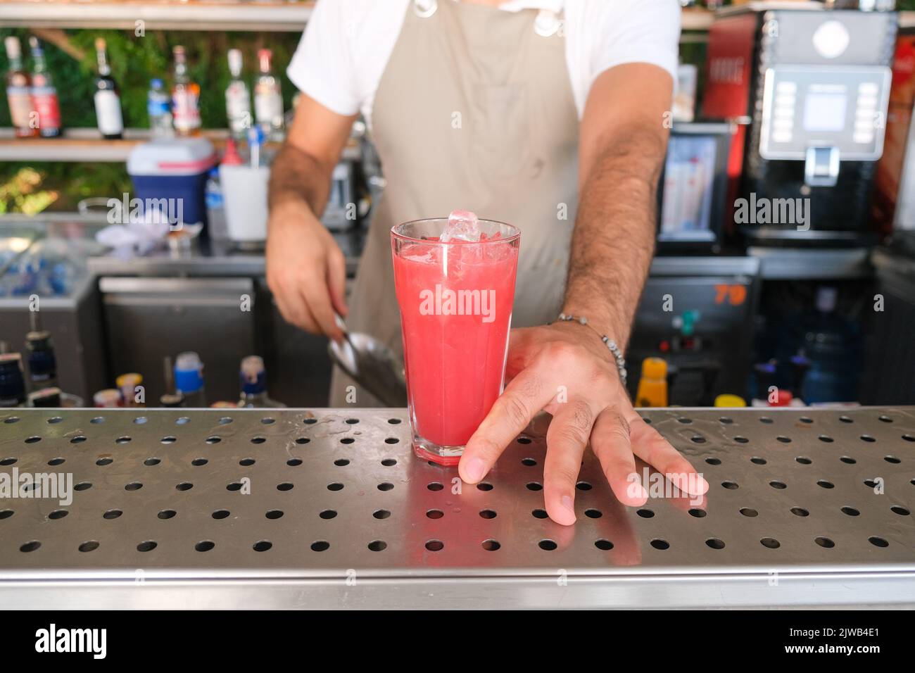 Main de barman servant un cocktail de fruits d'été rouges et violets frais avec glace au comptoir du bar par beau temps. Mise au point sélectionnée, faible profondeur de champ. Banque D'Images