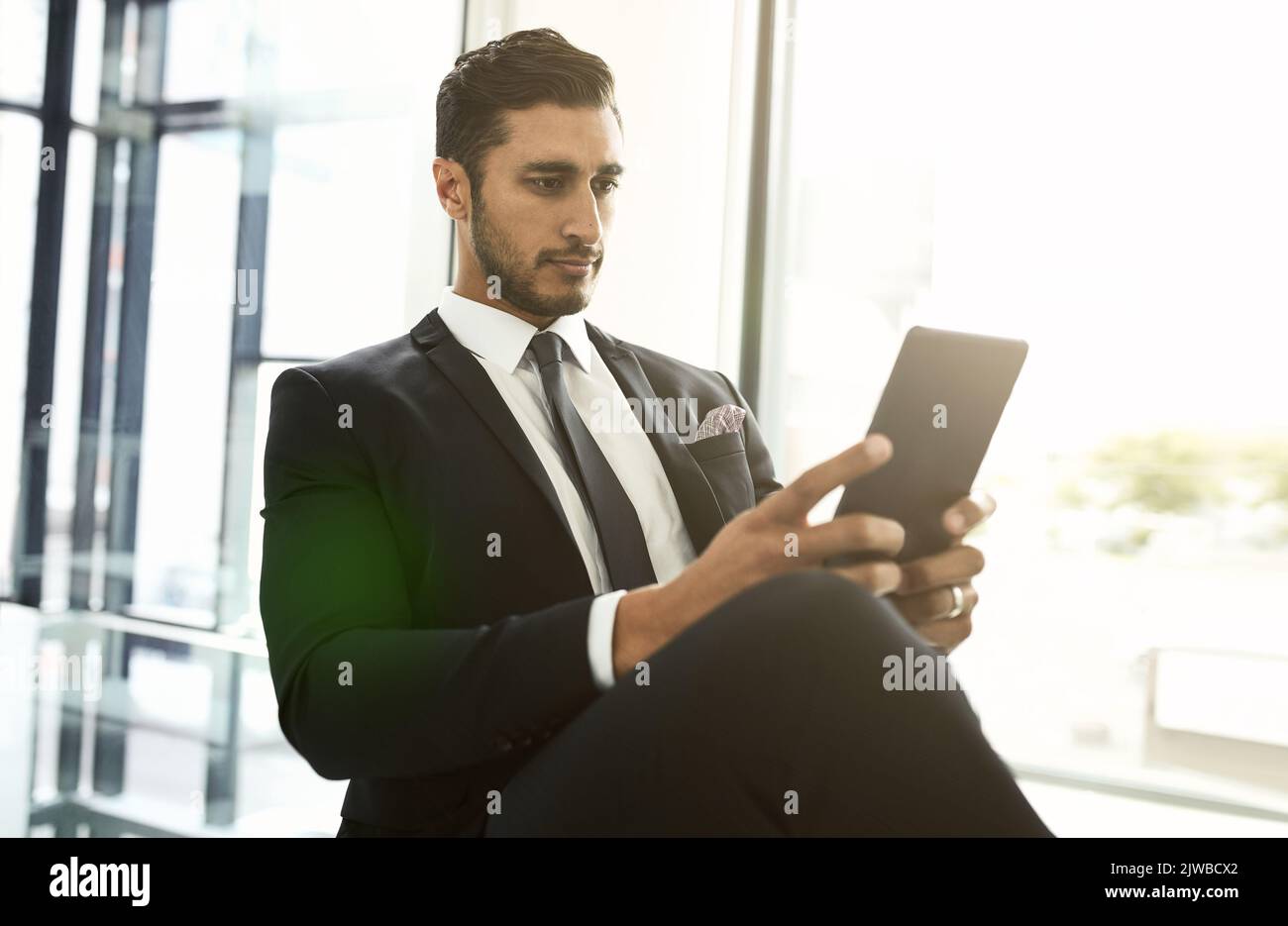 HES est capable de communiquer sans être lié à son bureau. Un homme d'affaires utilisant sa tablette tout en étant assis dans un bureau. Banque D'Images