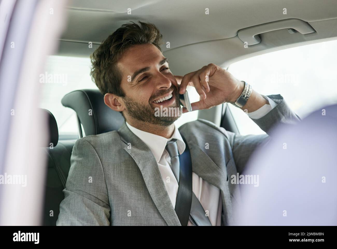 HES un homme d'affaires en mouvement. Un beau jeune homme d'affaires parlant sur un téléphone portable dans le siège arrière d'une voiture. Banque D'Images