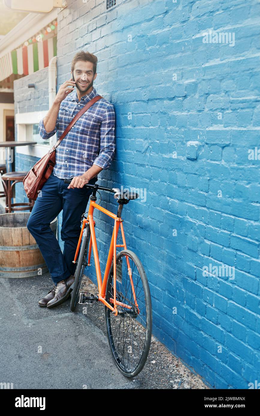 Je me suis happé sur mon vélo maintenant. Un beau jeune homme se penchait contre un mur avec son vélo parlant sur un téléphone portable. Banque D'Images