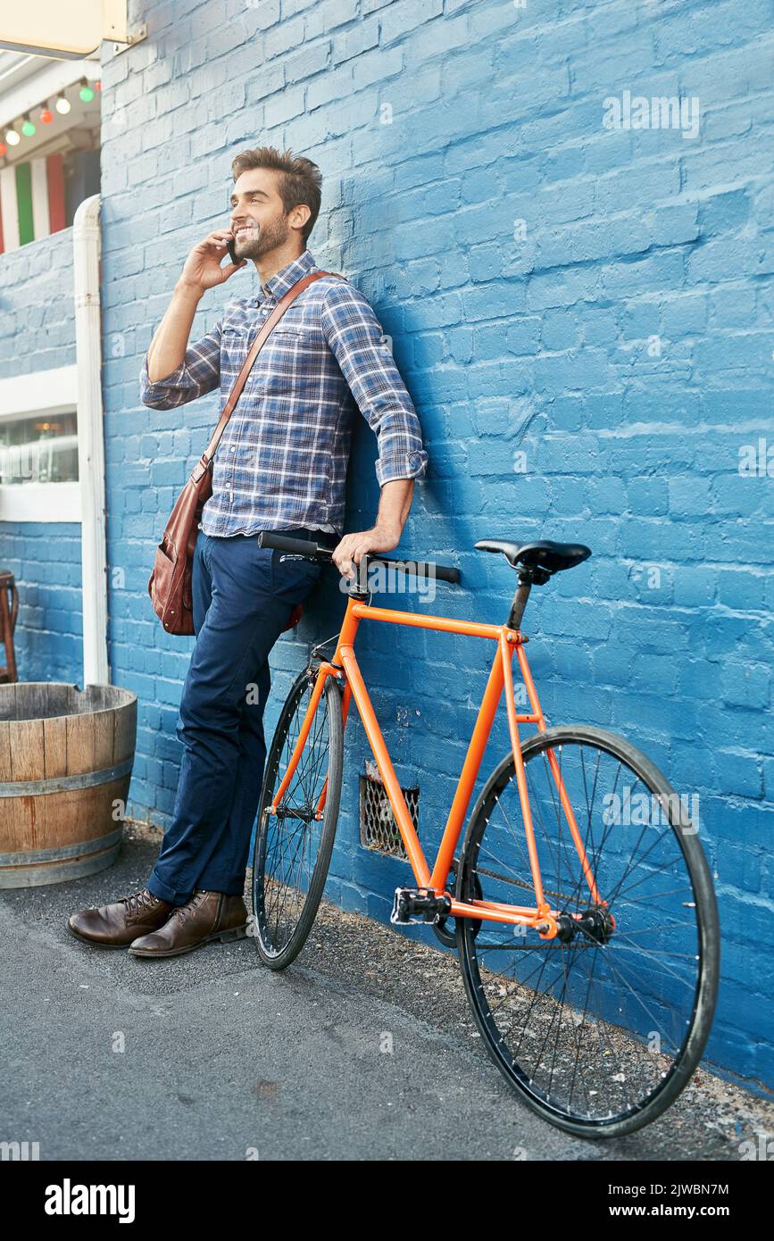 Je viens de me rendre au café. Un beau jeune homme se penchait contre un mur avec son vélo parlant sur un téléphone portable. Banque D'Images