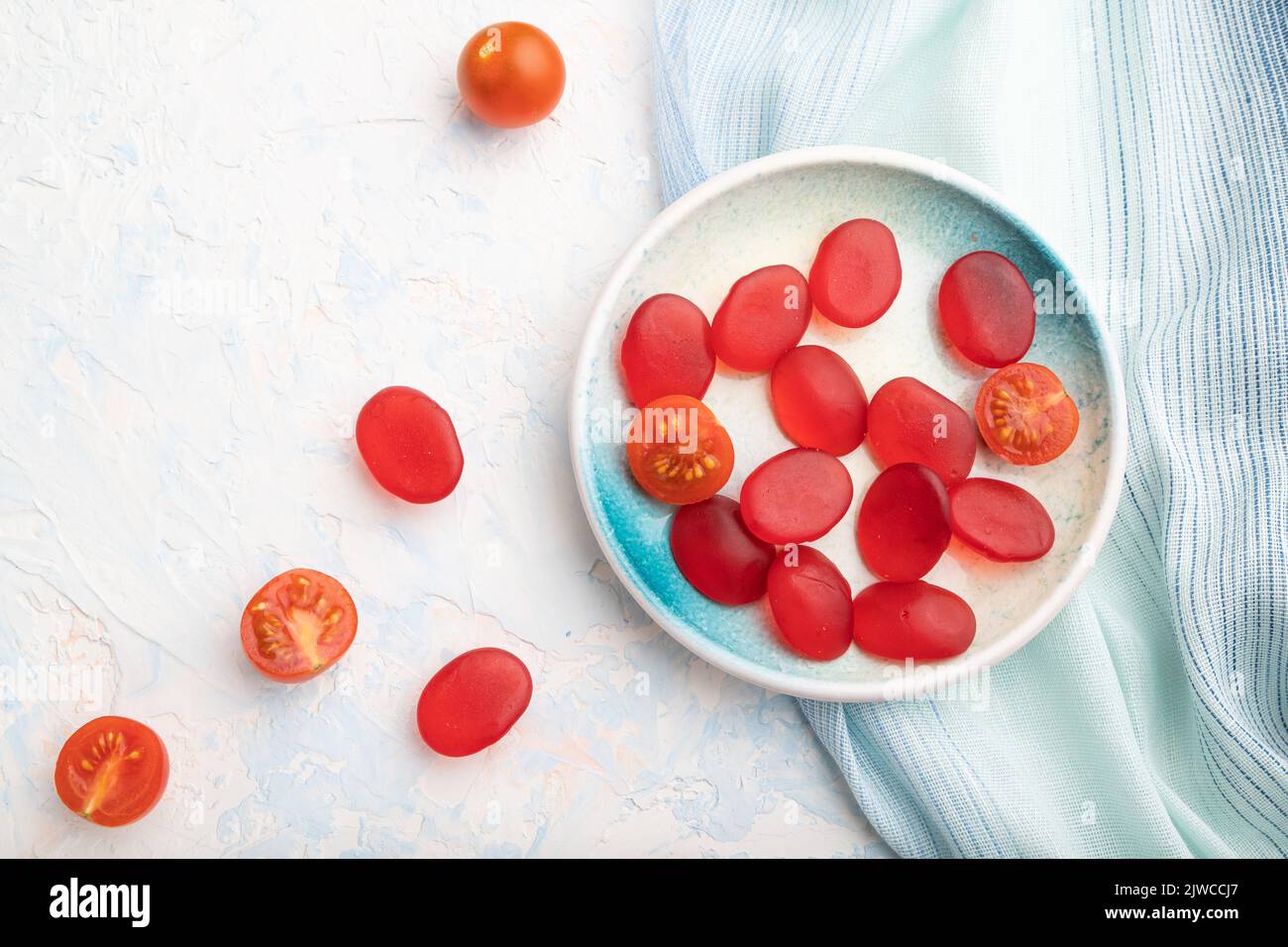Bonbons à la tomate en gelée sur fond de béton blanc et linge bleu. Gros plan, vue du dessus, plat. Banque D'Images