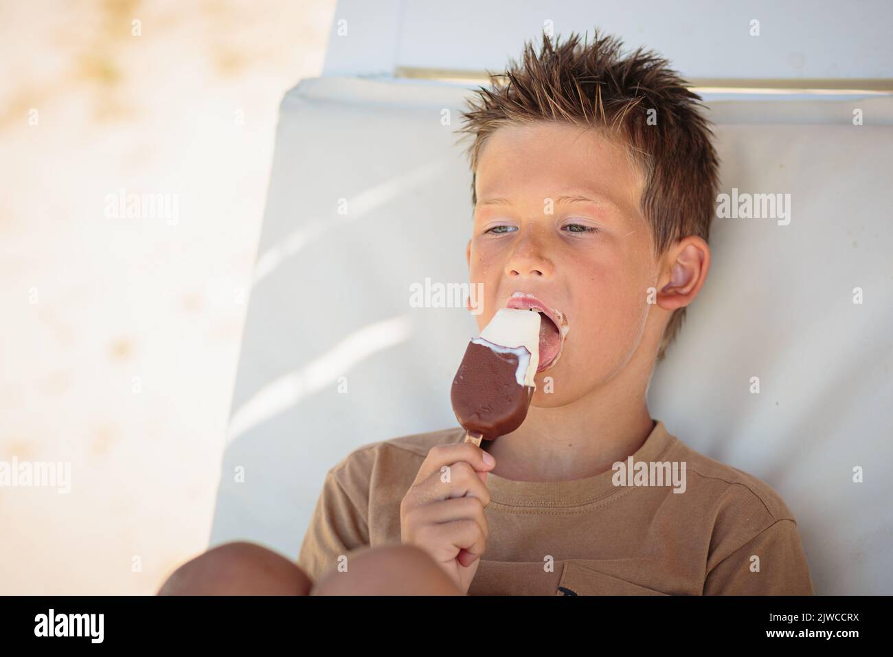 Beau garçon assis sur la plage et en train de manger de la glace Banque D'Images