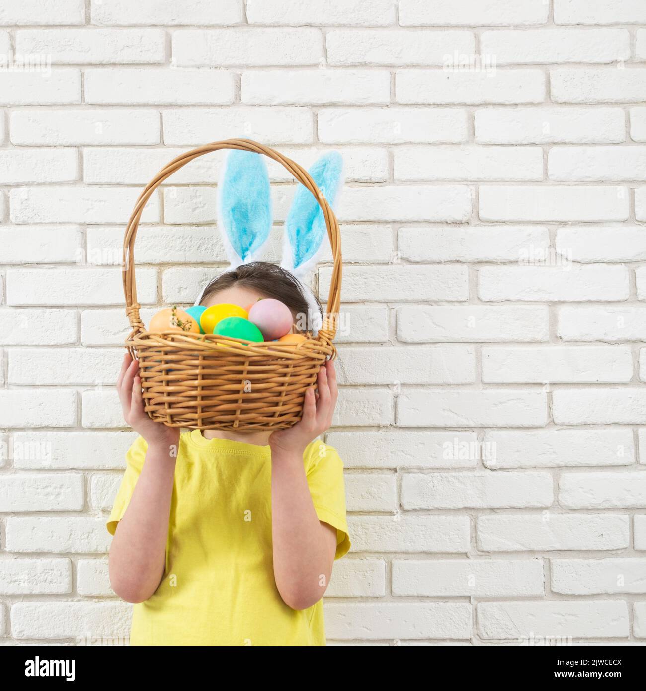 Garçon aux oreilles de lapin de Pâques avec panier en osier et œufs colorés. Copier l'espace Banque D'Images