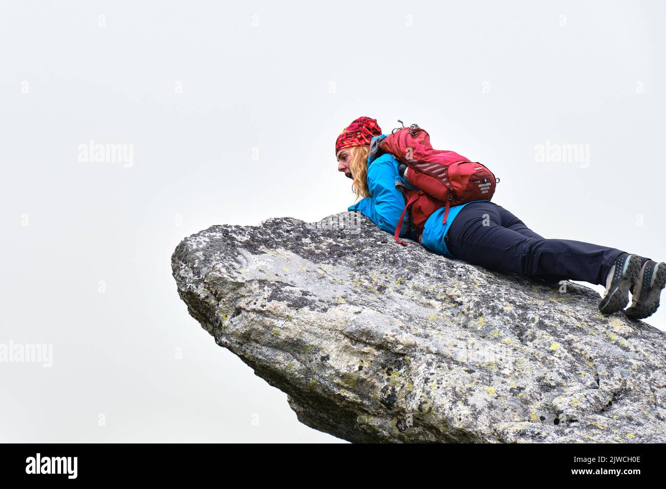 Femme randonneur avec sac à dos rouge se trouve au bord d'une falaise et regarde stupéfait et effrayé, isolé par le brouillard. Randonnée dans les montagnes des Hautes Tatras en Slovaquie. Banque D'Images