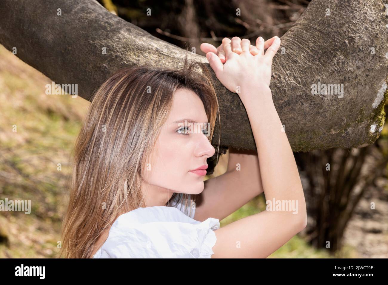 jolie femme blonde embrassant une branche d'arbre dans une robe blanche Banque D'Images