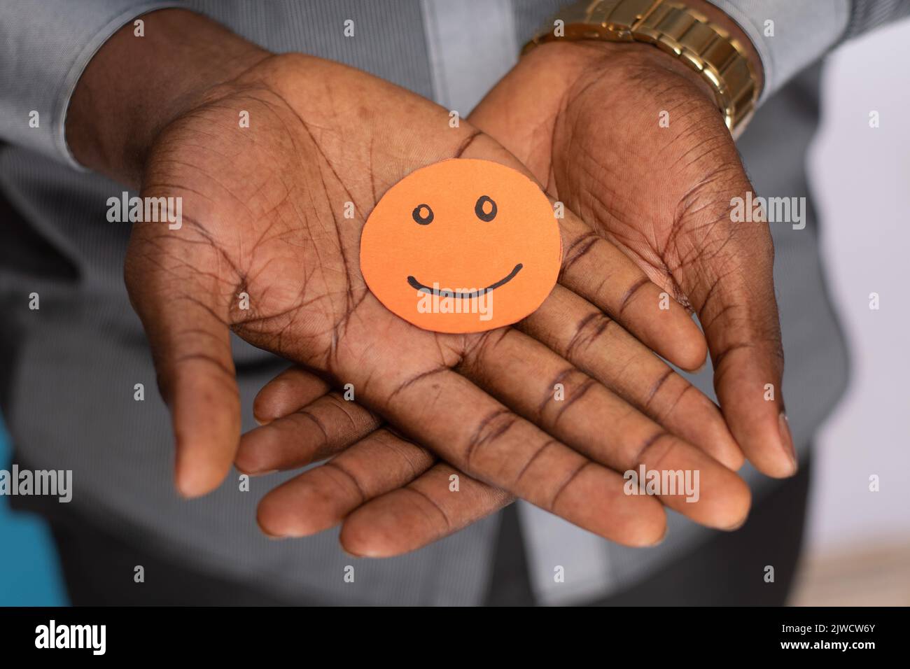 homme noir tenant une découpe en carton souriant visage emoji dans sa paume Banque D'Images