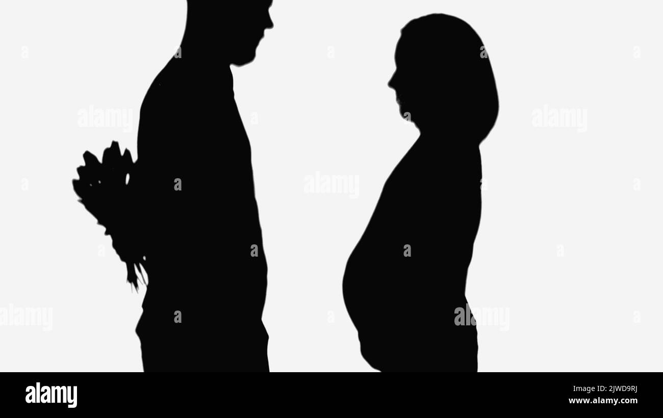 silhouette de l'homme tenant le bouquet derrière le dos près de la femme enceinte isolée sur blanc Banque D'Images