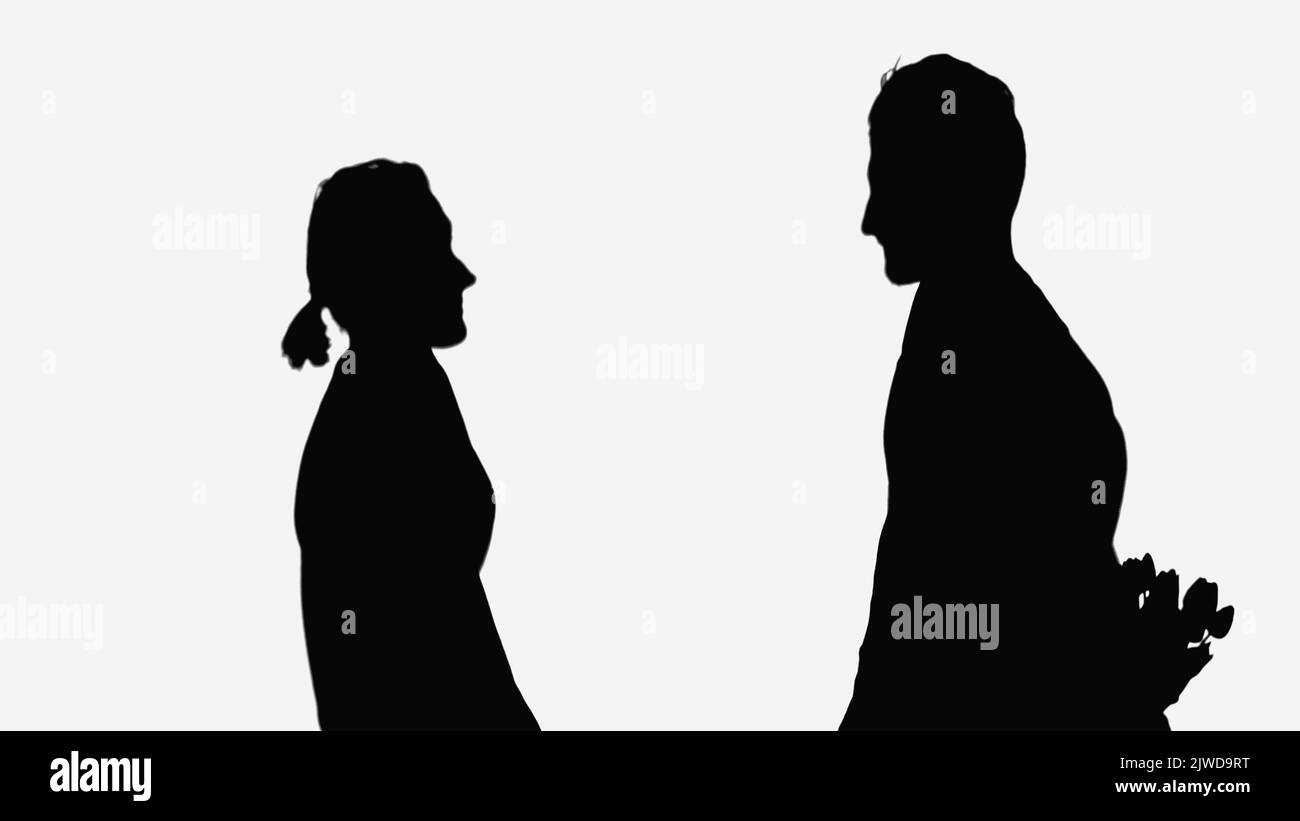 silhouette noire de l'homme tenant le bouquet derrière le dos près de la femme isolée sur blanc Banque D'Images