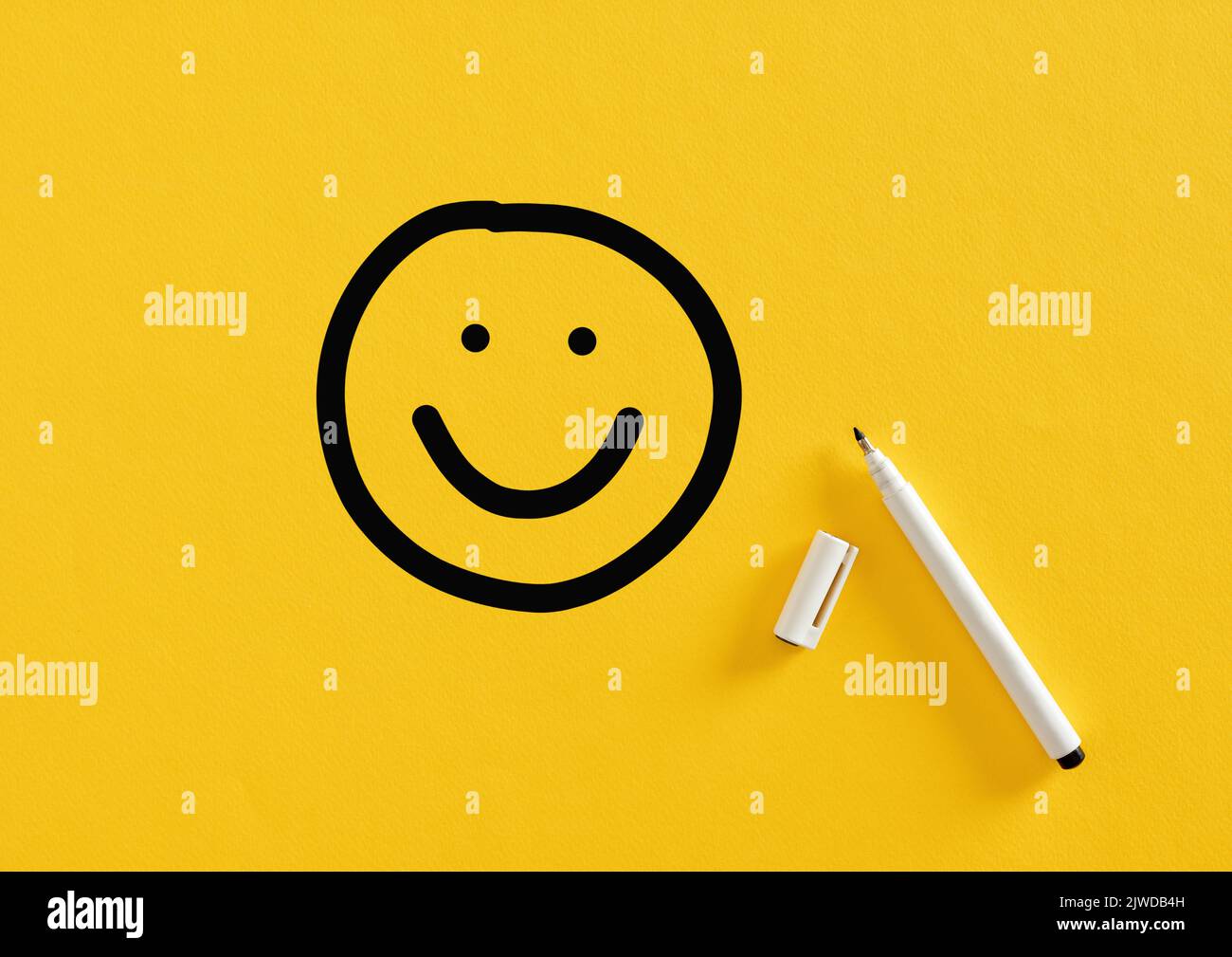 Dessin souriant visage heureux dessiné à la main avec un marqueur feutre sur fond jaune. Satisfaction de la clientèle, évaluation du service ou du produit Banque D'Images