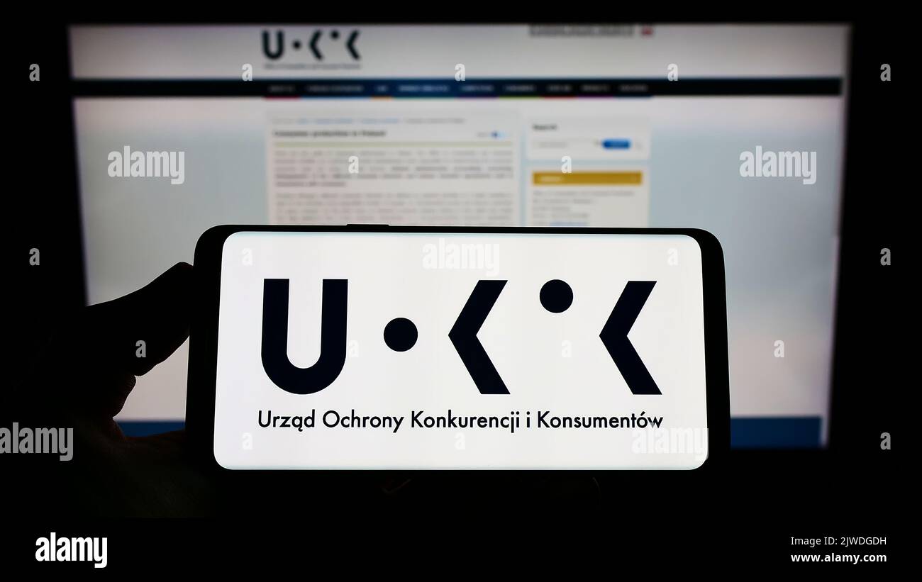 Personne tenant un smartphone avec le logo de l'autorité polonaise de la concurrence UOKiK sur l'écran devant le site Web. Mise au point sur l'affichage du téléphone. Banque D'Images