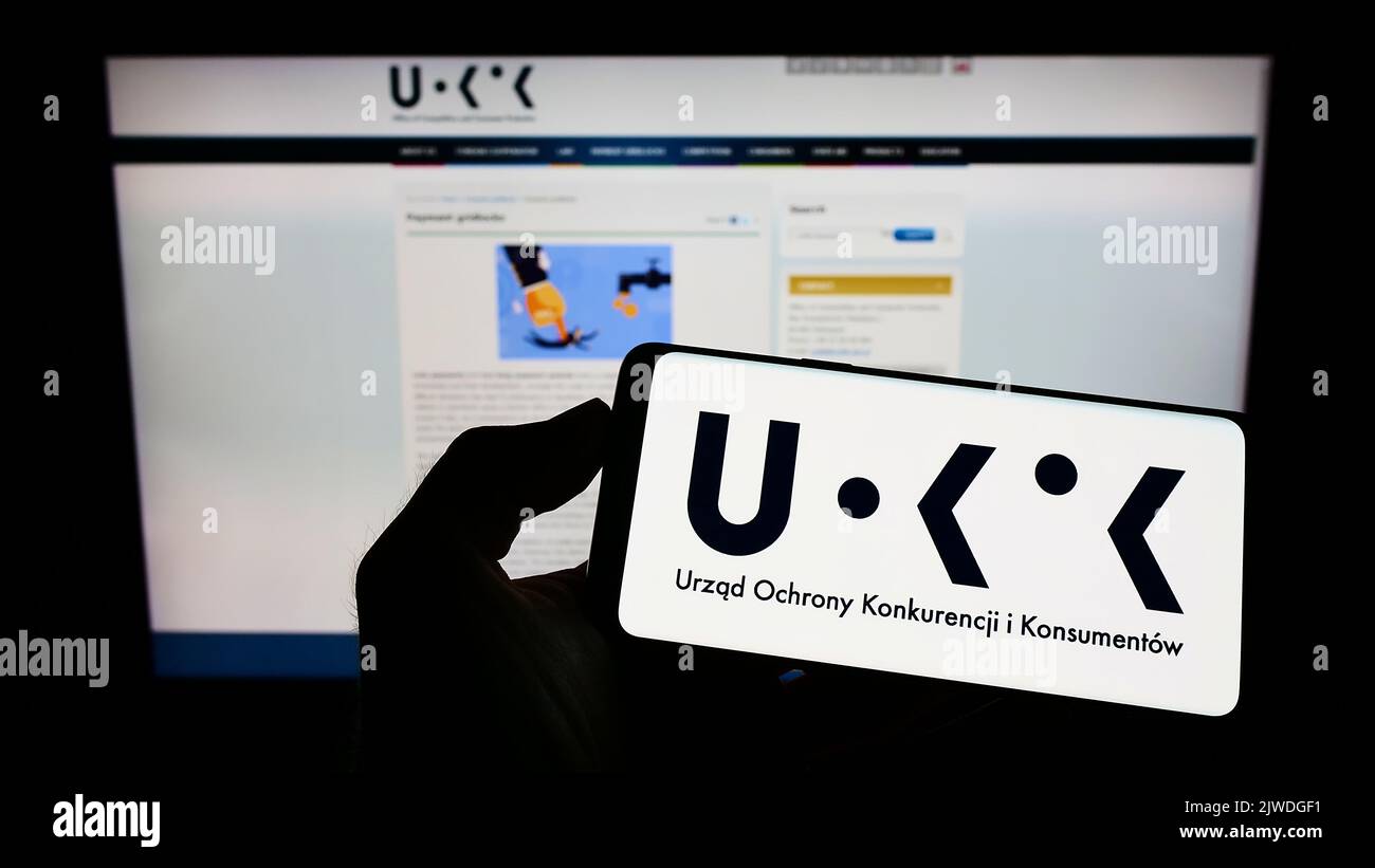 Personne tenant un téléphone portable avec le logo de l'autorité polonaise de la concurrence UOKiK à l'écran en face de la page web. Mise au point sur l'affichage du téléphone. Banque D'Images