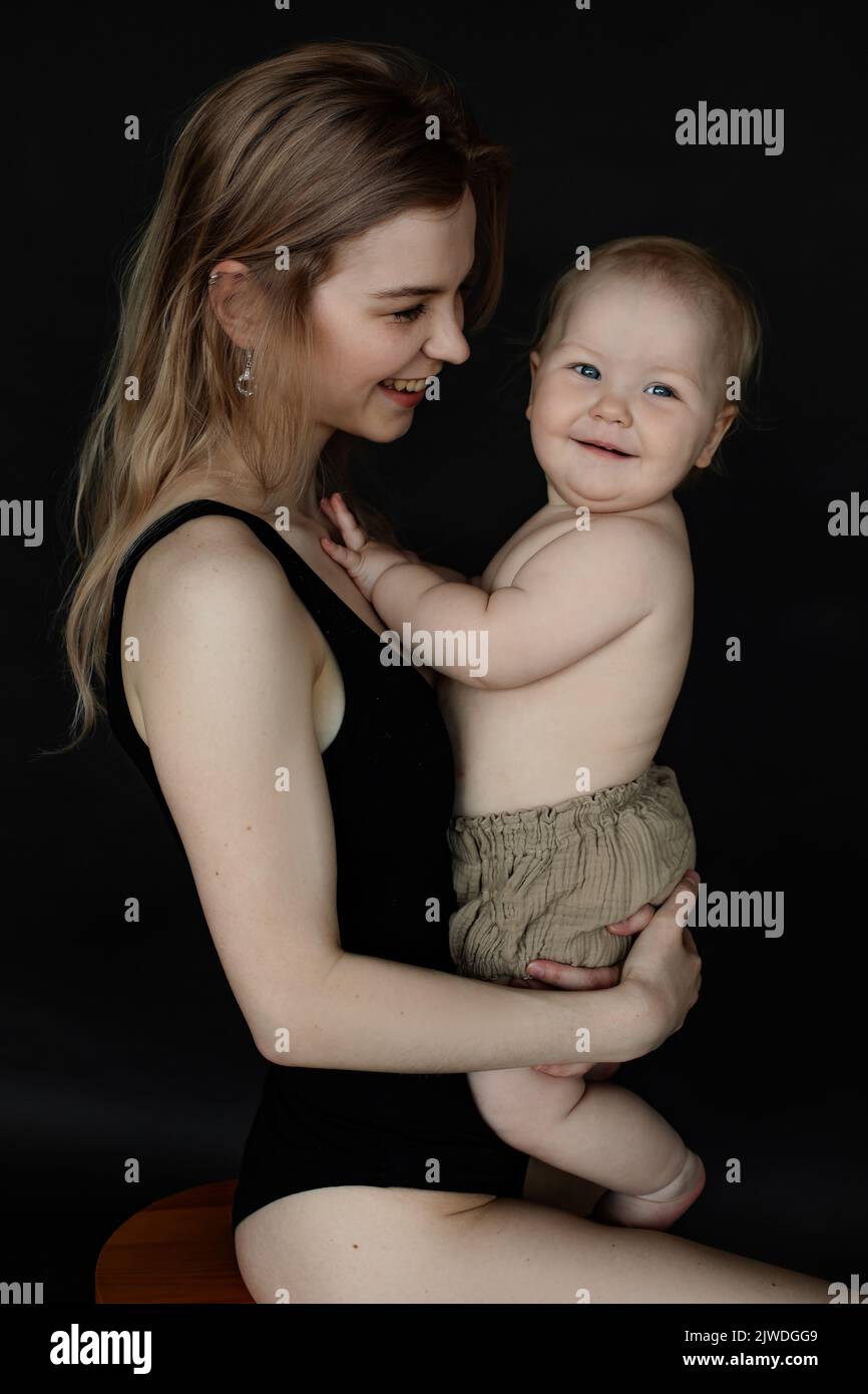 Vertical gros plan blond riant femme, mère tient enfant, bébé regarde enfant souriant dans couches. Garde d'enfants Banque D'Images