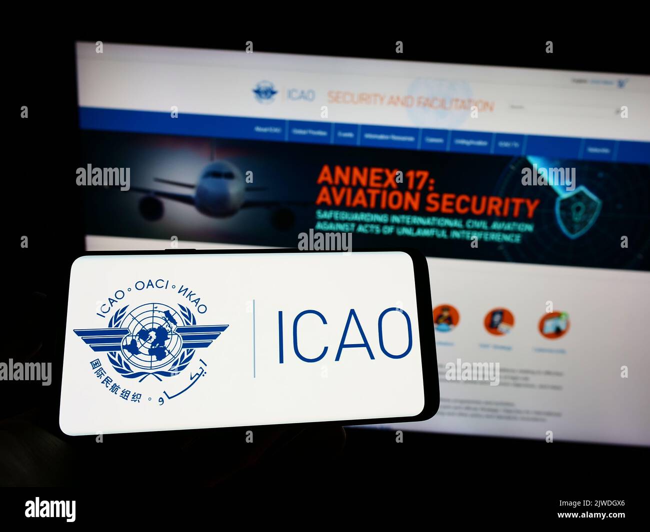 Personne tenant un téléphone portable avec le logo de l'Organisation de l'aviation civile internationale (OACI) à l'écran en face de la page Web. Mise au point sur l'affichage du téléphone. Banque D'Images