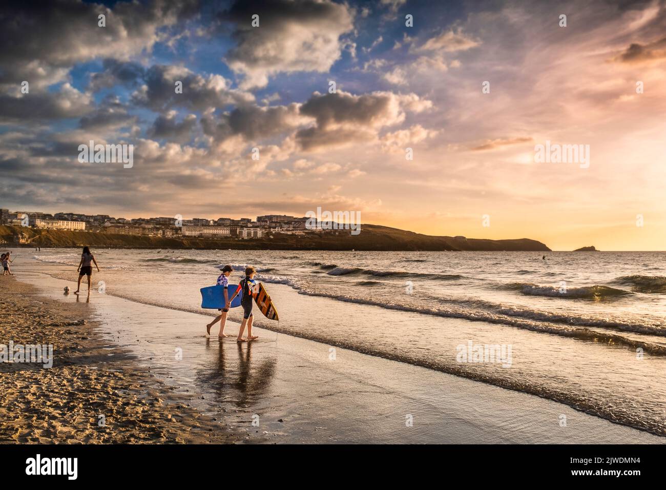 Deux jeunes garçons portant leurs planches de bodyboard et marchant dans la mer à Fistral dans la lumière dorée le soir à Newquay dans Cornwall en t. Banque D'Images