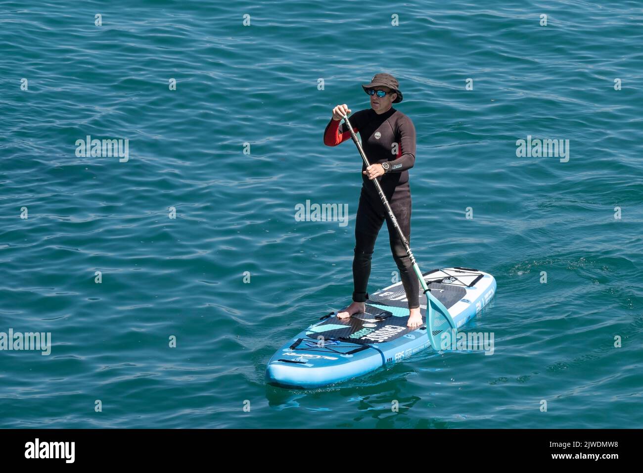 Un holidaymaker debout sur un stand Up Paddleboard à Newquay Bay, en Cornouailles, en Angleterre, au Royaume-Uni. Banque D'Images