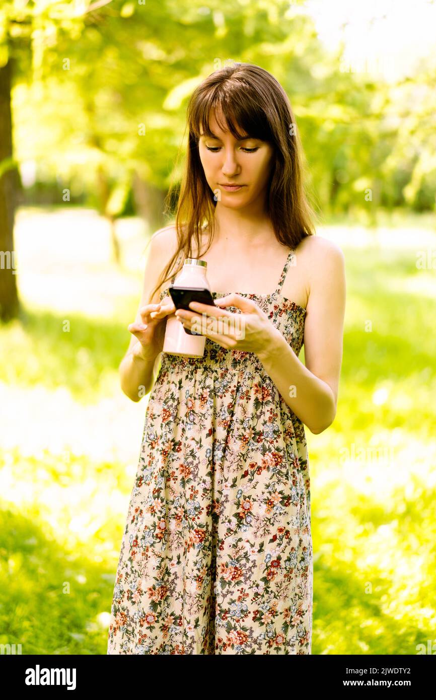 Une jeune fille brune caucasienne lit un message sur son téléphone. Portrait dans le parc. Banque D'Images